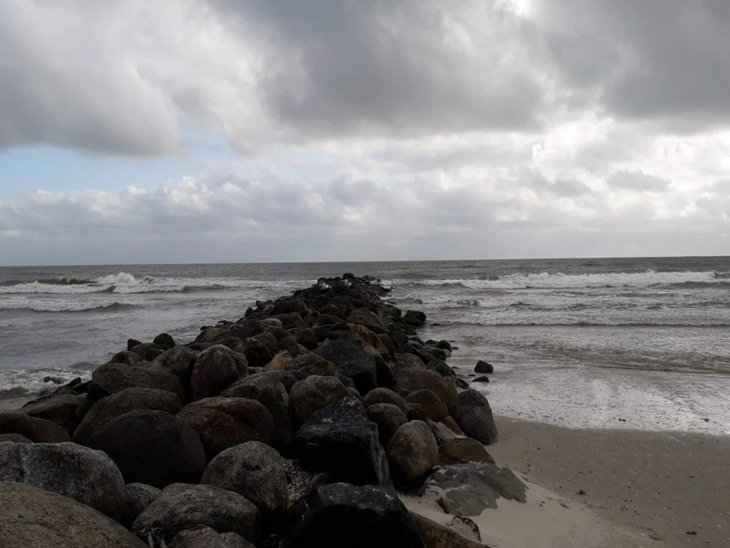 A rocky breakwater extending into the sea with waves crashing against it.