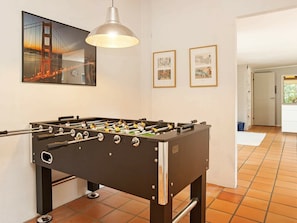 A room with a foosball table, a pendant light, and framed pictures on the wall.