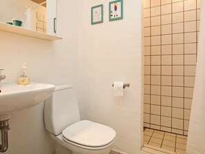 A bathroom with a white sink, toilet, and shower area. There are two framed pictures on the wall.