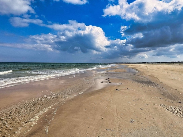 A beach with a wide sandy shore, waves, and a partly cloudy sky.