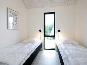 A bedroom with two single beds, a framed bird illustration on the wall, and a window with a view of greenery outside.