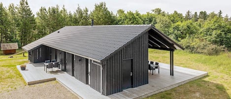 A modern, single-story building with a sloped roof, a covered outdoor seating area, and a gravel deck.
