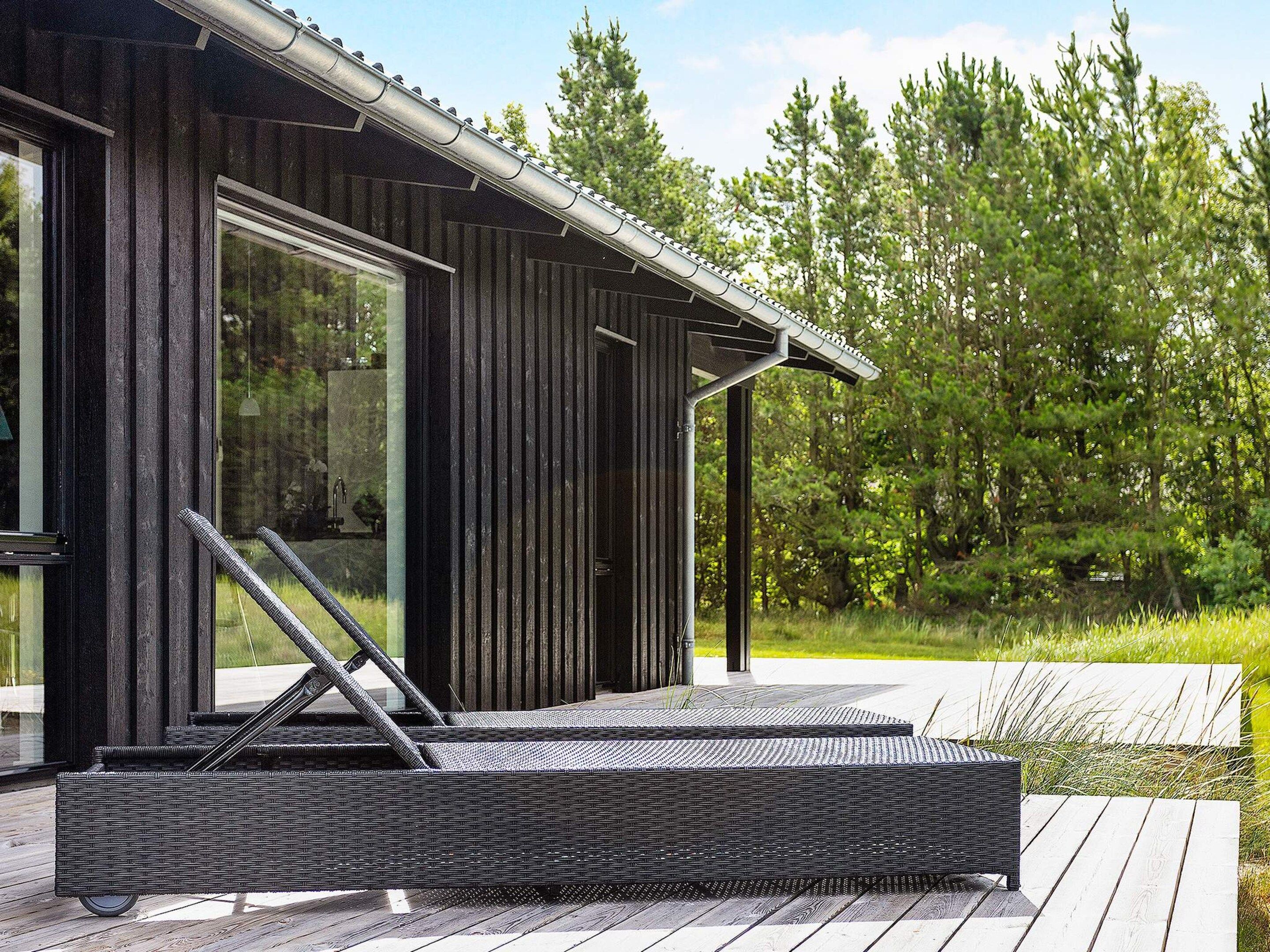 Un espace extérieur moderne aménagé avec des meubles de jardin, comprenant un fauteuil de relaxation en osier et une table, situé à côté d’un bâtiment doté de grandes fenêtres et d’une porte.