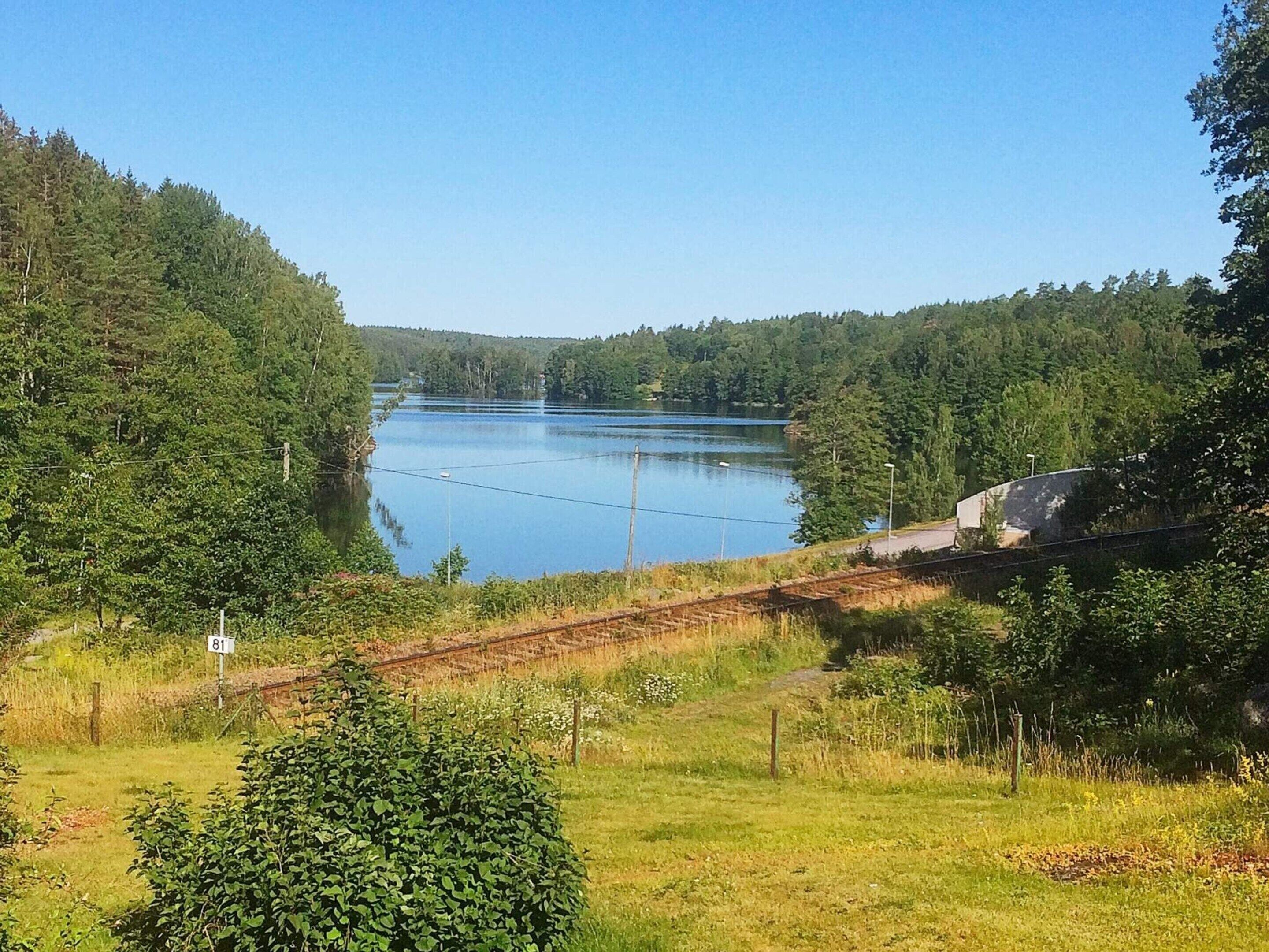 A lake surrounded by dense forest, with a railway track running parallel to the water.