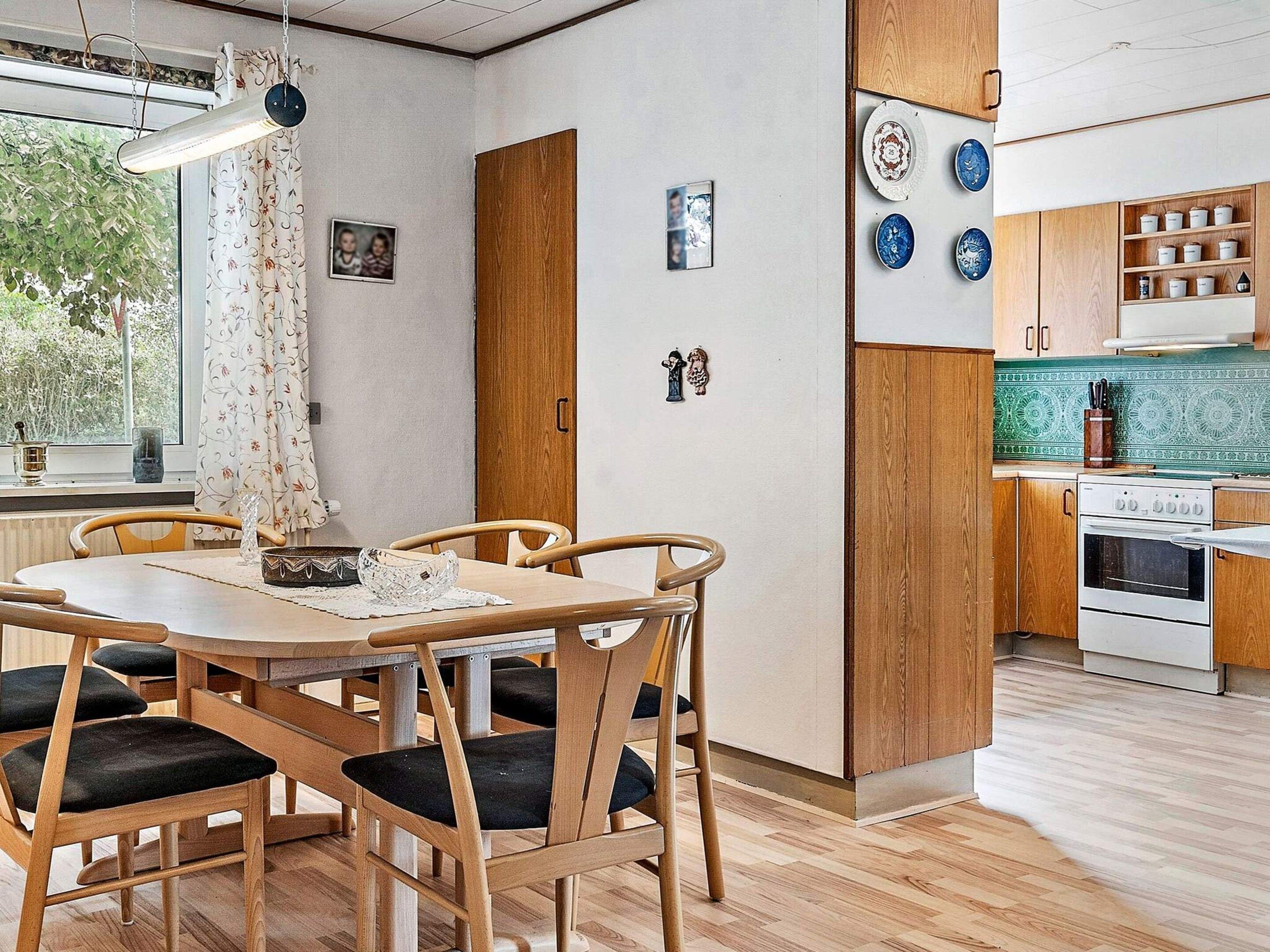 Una cocina moderna con armarios de madera, horno integrado y comedor con mesa y sillas de madera.