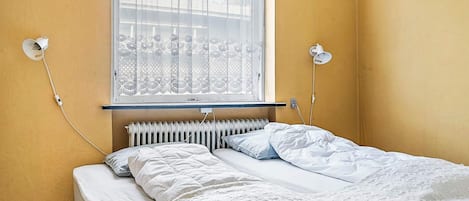 A single bed with a white duvet and pillows, a radiator below the window, and two wall-mounted lamps.