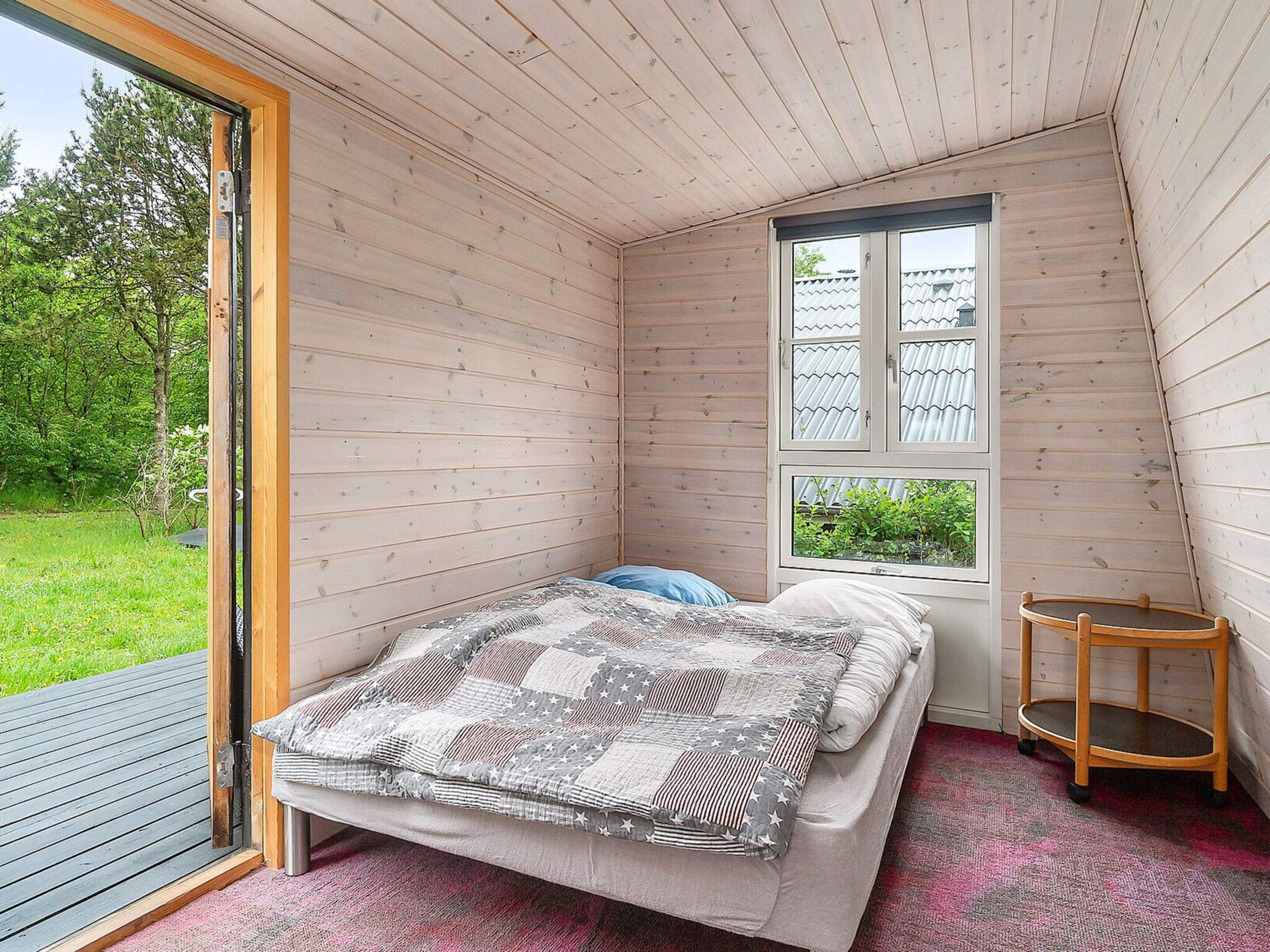 Um quarto pequeno e acolhedor com uma cama, uma janela e uma cadeira de madeira.