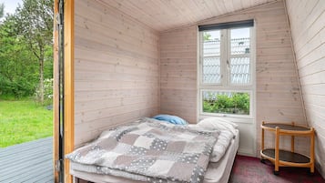 Um quarto pequeno e acolhedor com uma cama, uma janela e uma cadeira de madeira.