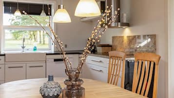 Uma cozinha moderna com luminárias pendentes, uma mesa de jantar e um vaso com ramos.