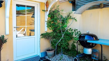 Une terrasse avec un barbecue, une porte, un petit arbre et une plante en pot.