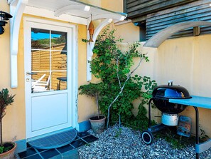 A patio with a grill, a door, a small tree, and a potted plant.