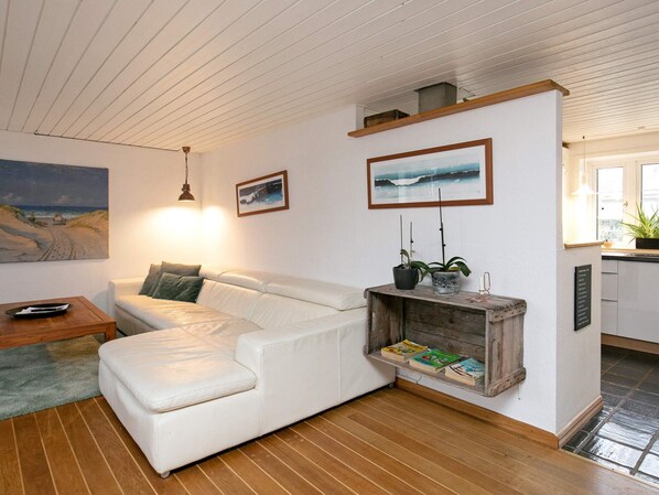 A cozy living room with a white leather sofa, wooden flooring, a coffee table, and a fireplace with books.