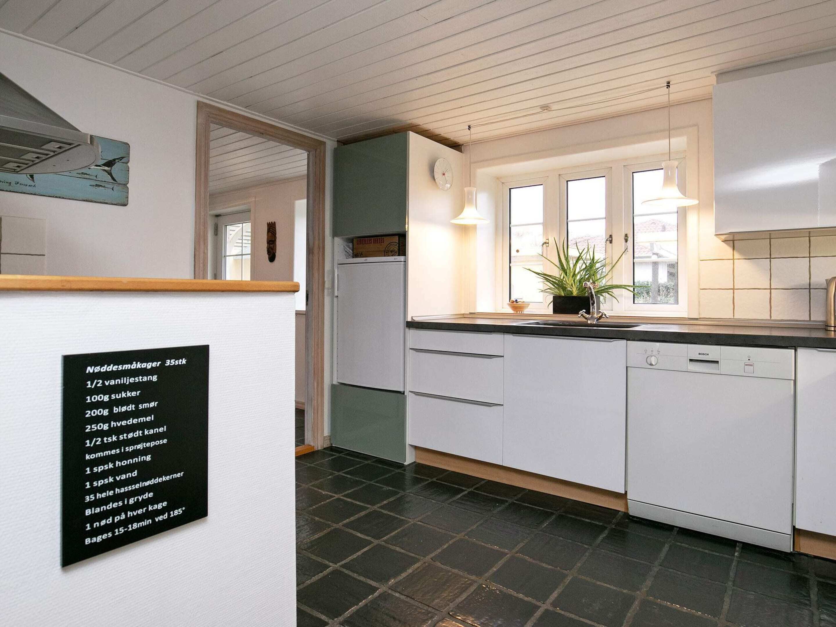 A modern kitchen with white cabinets, a Bosch dishwasher, a refrigerator, and a window with a view.