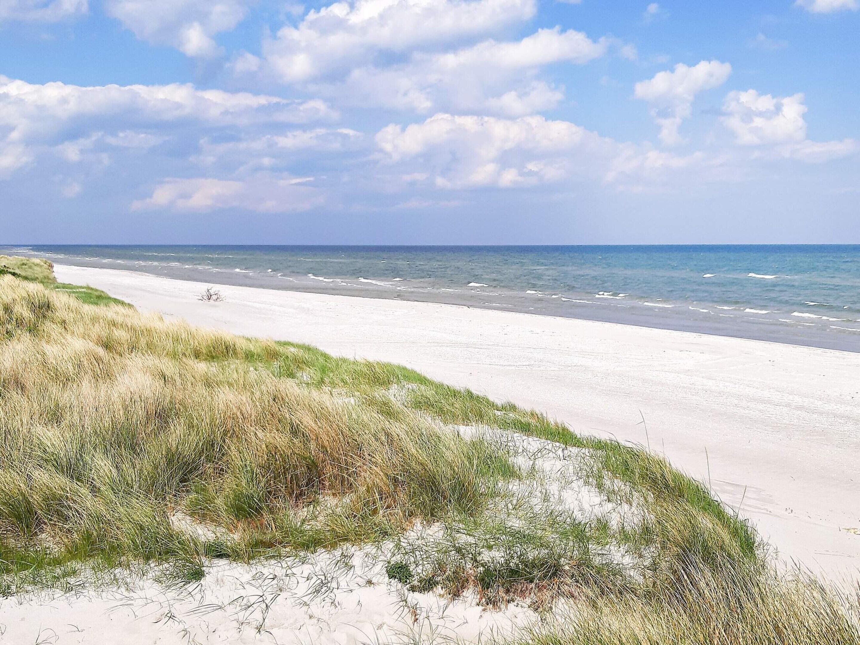 Ein Strand mit weißem Sand, Wellen im Ozean und grasbewachsenen Dünen.