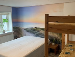 Un dormitori amb un llit, una finestra amb vista a la platja i un mural del capvespre.