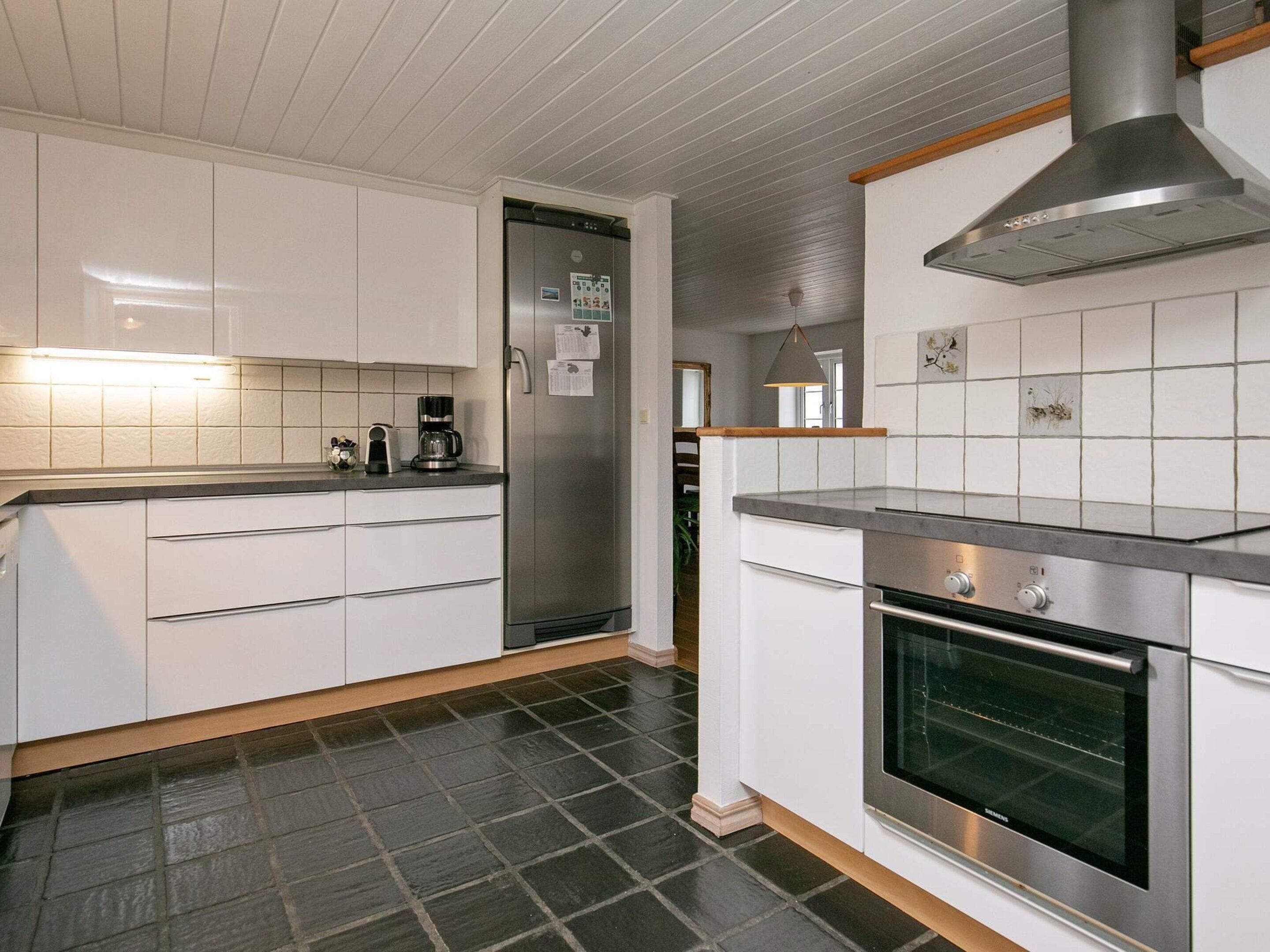 A modern kitchen with white cabinetry, a stainless steel refrigerator, a built-in oven, and a tiled backsplash.