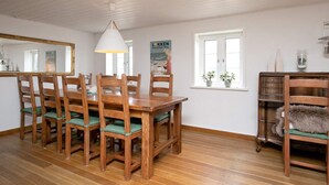 A dining area with a wooden table and chairs, a hanging light fixture, a mirror, and a window with potted plants. - Holiday Home in LÃ¸kken (Lokken)