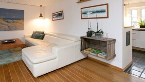 A cozy living room with a white leather sofa, wooden floor, and a small wooden shelf with books. - Holiday Home in LÃ¸kken (Lokken)
