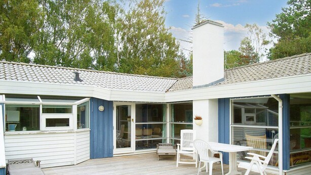 A covered patio with a white table and chairs, a wooden deck, and a white building with a blue door and windows. - Holiday Home in NykÃ¸bing Sj (Nykobing Sjaelland)