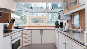 A modern kitchen with white cabinets, a built-in oven, a coffee maker, and a window overlooking a forest. - Holiday Home in NykÃ¸bing Sj (Nykobing Sjaelland)