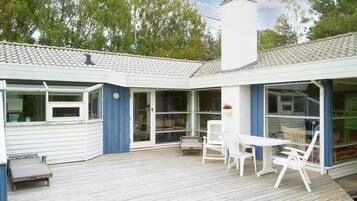 A covered outdoor area with a wooden deck, white furniture, and a white chimney.