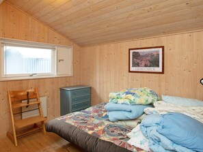 A bedroom with a wooden ceiling, a bed with multiple pillows, a dresser, a chair, and a window with a view of a fence. - Holiday Home in Nykøbing Sj (Nykobing Sjaelland)