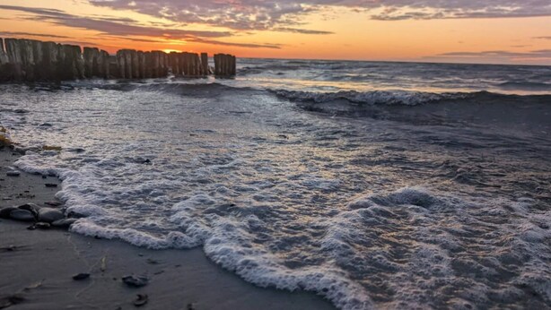 Une plage avec des vagues, une structure en bois et un coucher de soleil.