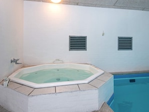 A hot tub with a tiled surround, a pool, and a wall with two vents.