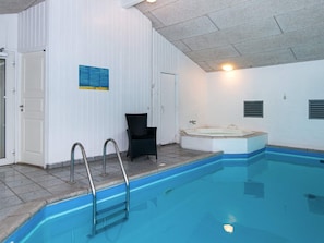 An indoor swimming pool with a hot tub, a chair, and a ladder.