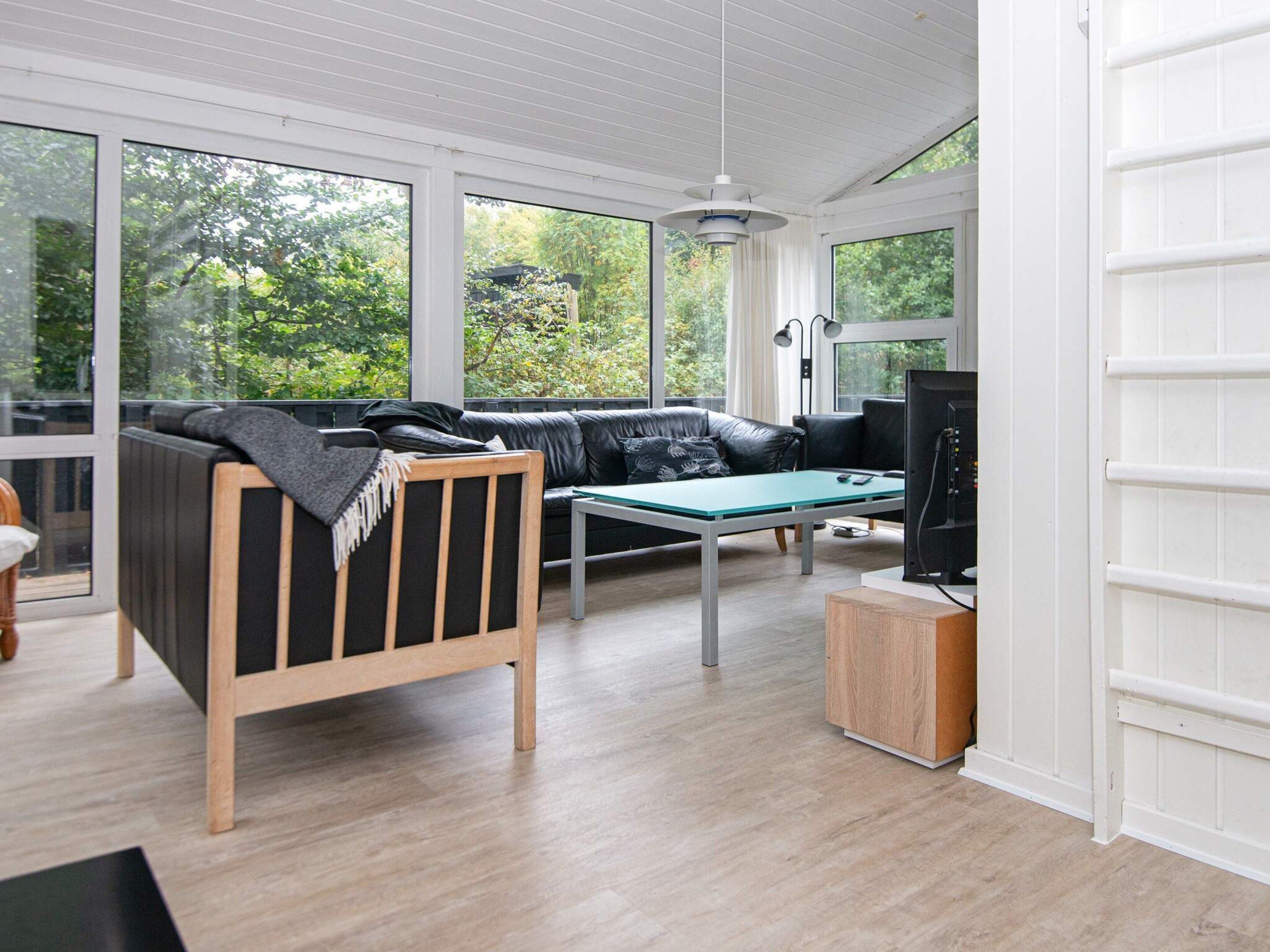 Ein modernes Wohnzimmer mit einem schwarzen Ledersofa, einem hölzernen Bettgestell, einem Glastisch und einem Fernseher auf einem Holzboden.
