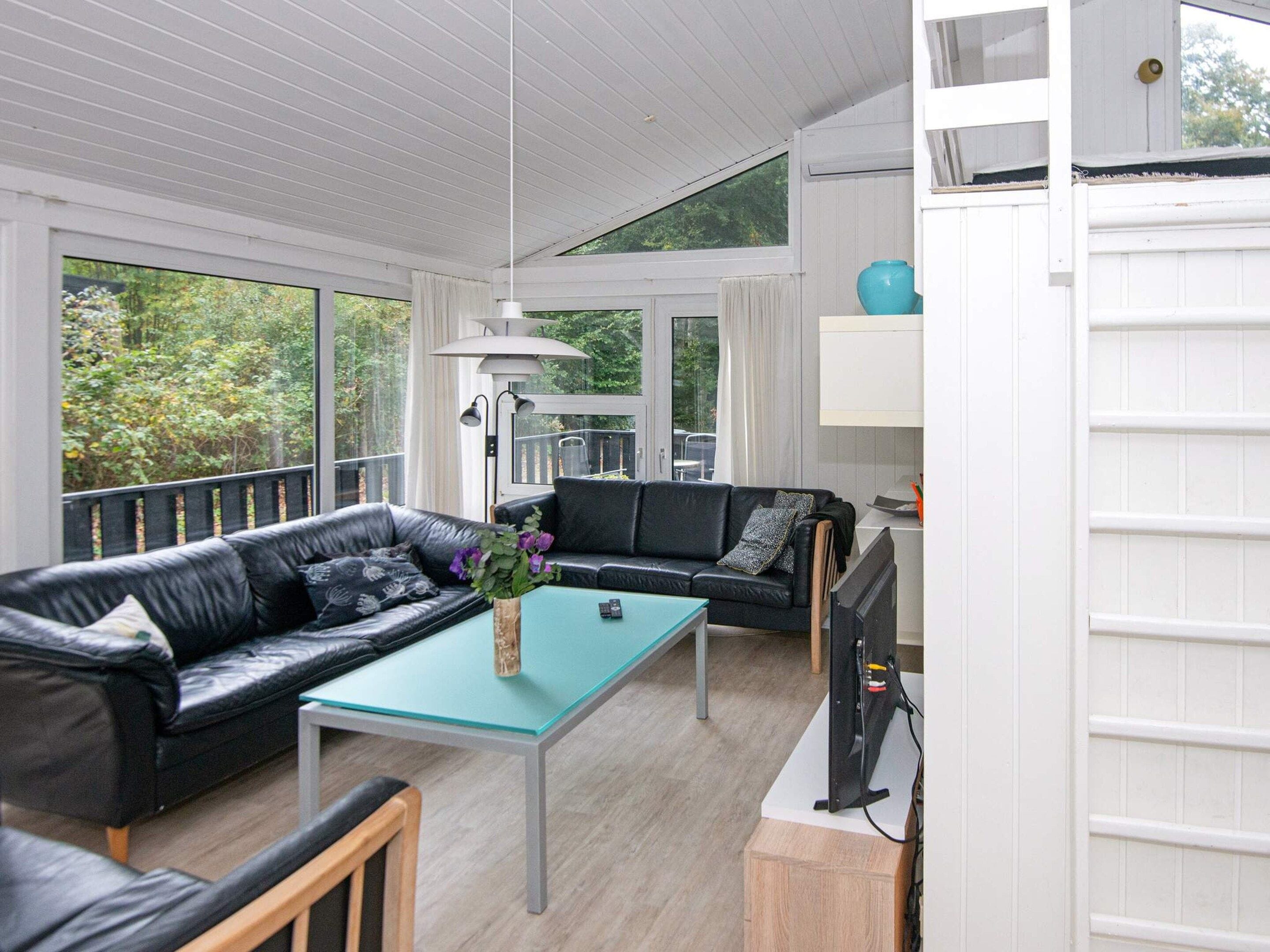 A modern living room with a glass coffee table, two black leather sofas, and a television.