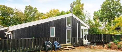 A modern wooden cabin with a large window, a door, and a small porch area with chairs.