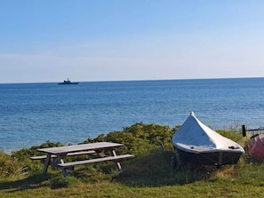 A picnic table and a tent by a body of water with a ship in the distance.