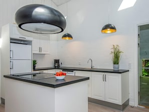 A modern kitchen with white cabinetry, a central island, black countertops, and pendant lighting.