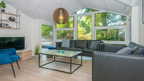 A modern living room with a large TV, a sofa, a coffee table, and a hanging light fixture. - 4 Star Holiday Home in Glesborg (Glesborg)