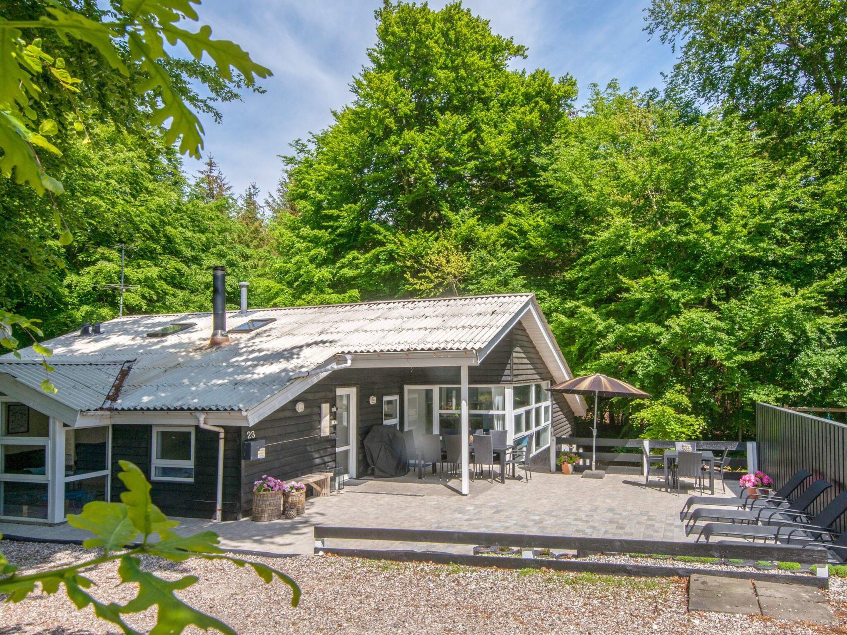 Ein rustikales Blockhaus mit Metalldach, einer überdachten Terrasse mit Sitzgelegenheiten und einer umliegenden Waldlandschaft.