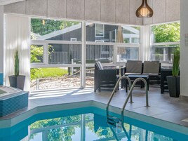 An indoor swimming pool with a clear view of the outdoors, surrounded by wicker furniture and a glass barrier.