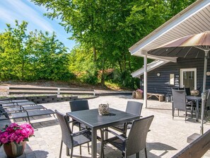 An outdoor patio area with a table and chairs, a covered seating area, and a view of a wooded area. - 4 Star Holiday Home in Glesborg (Glesborg)