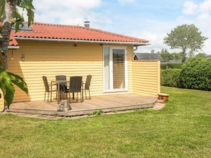 En gul bygning med rødt tag, træterrasse og en glasdør.