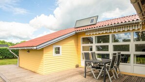 A yellow building with a red roof, a covered patio with a table and chairs, and a large window. - 6 Person Holiday Home in Hadsund (Hadsund)
