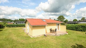A single-story yellow building with a red roof, a patio with a table and chairs, and a small vehicle parked outside. - 6 Person Holiday Home in Hadsund (Hadsund)