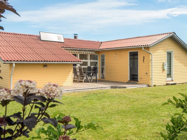 A yellow building with a red roof, a covered patio with chairs, and a door leading to a garage.