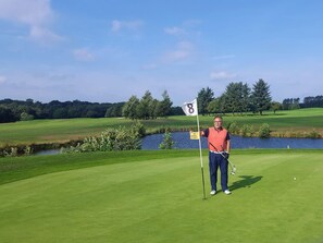 Un campo de golf con una bandera marcada '8', un estanque y árboles al fondo.