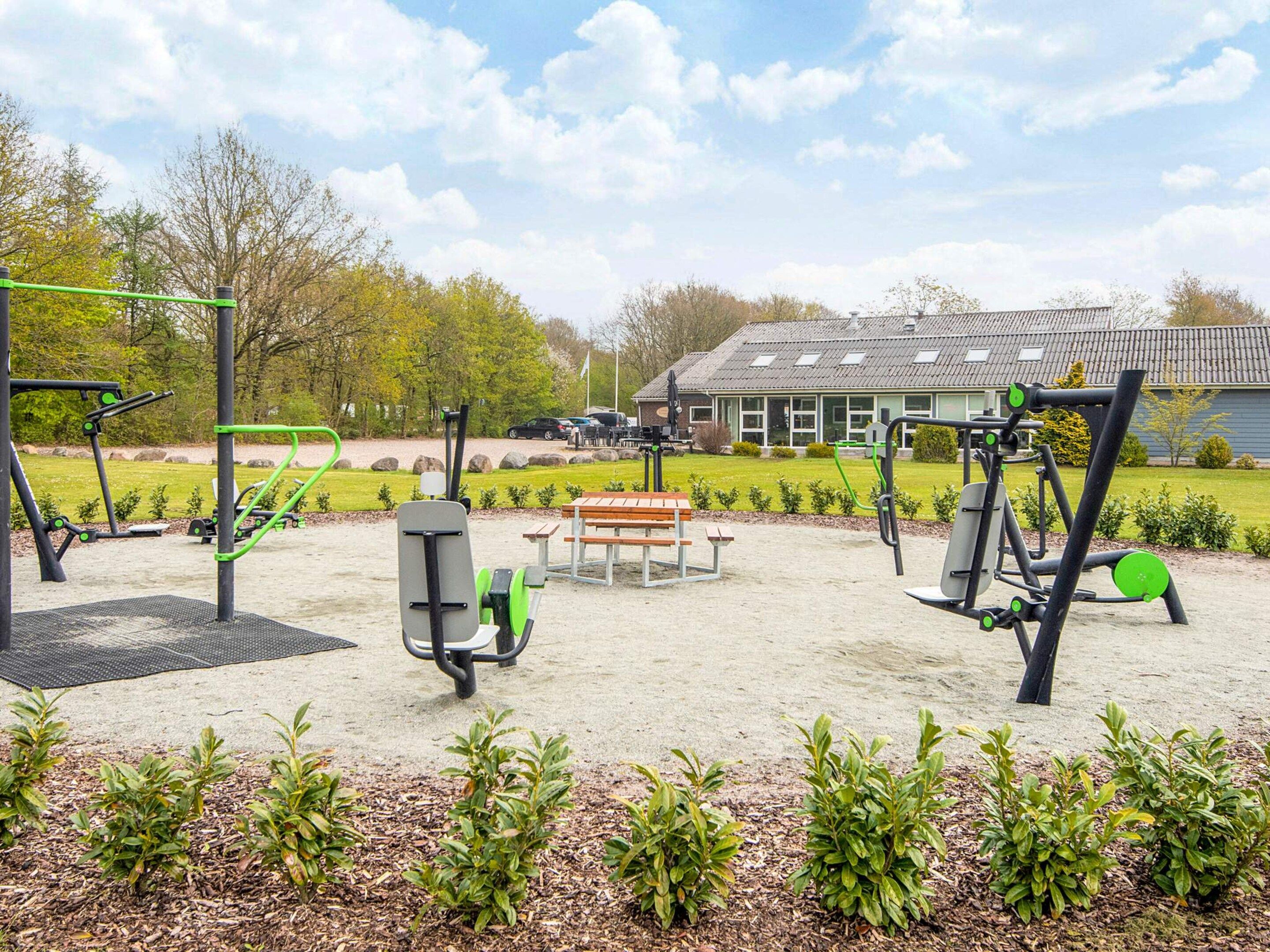An outdoor gym area with exercise equipment, a picnic table, and a building in the background.