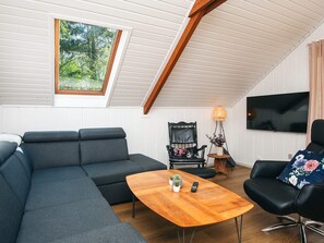 A modern living room with a sectional sofa, a wooden coffee table, a black armchair, and a television mounted on the wall. - 6 Person Holiday Home in Toftlund (Toftlund)