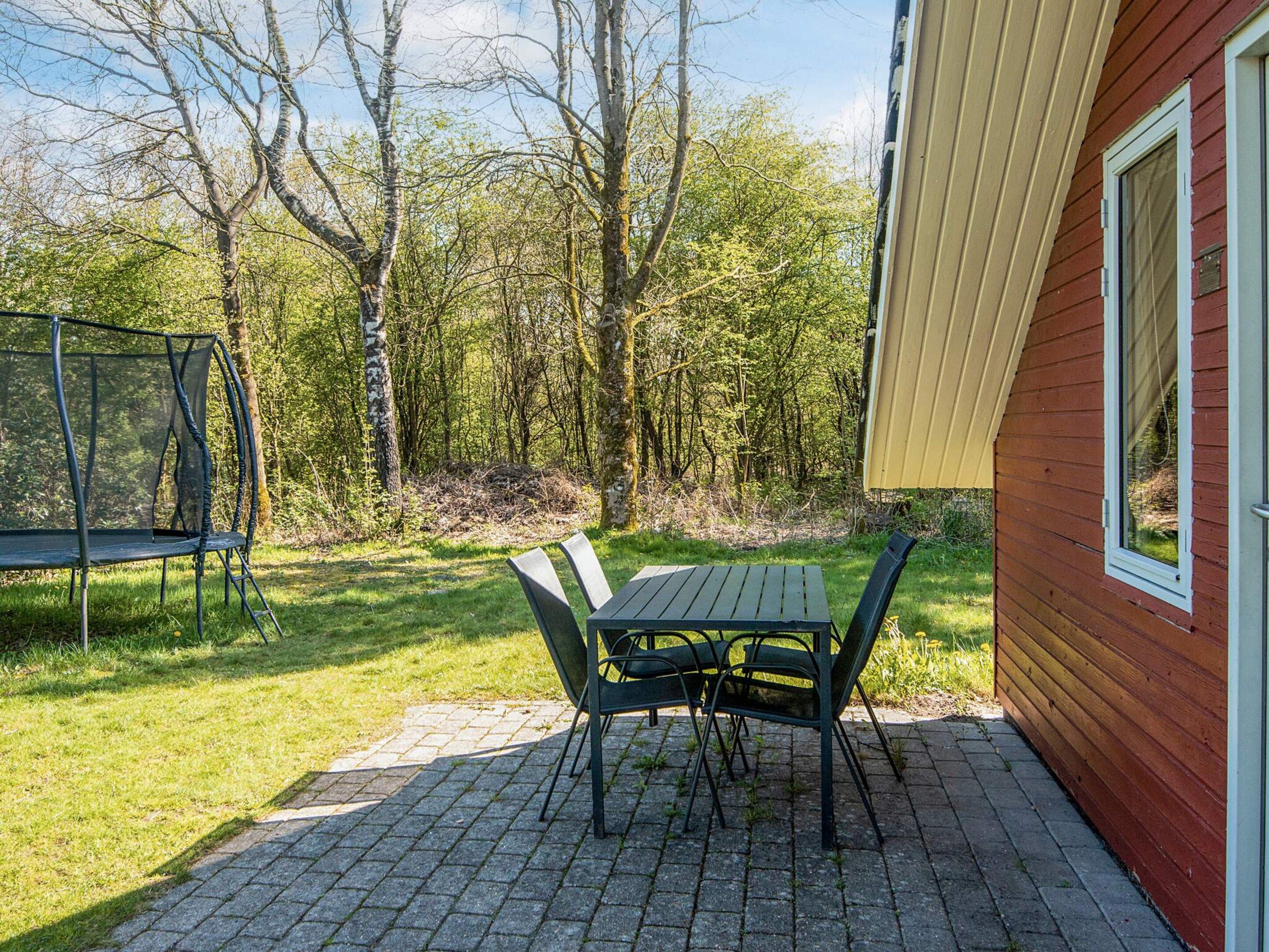 An outdoor patio with a table and chairs, surrounded by a grassy area and trees.