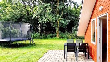 Eine Terrasse mit Trampolin, Tisch und Stühlen, umgeben von einem Holzgebäude und Bäumen.