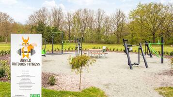Un'area fitness all'aperto con attrezzature per esercizi, un cartello segnaletico e un tavolo da picnic.