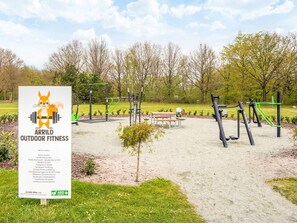 An outdoor fitness area with exercise equipment, a signboard, and a picnic table.
