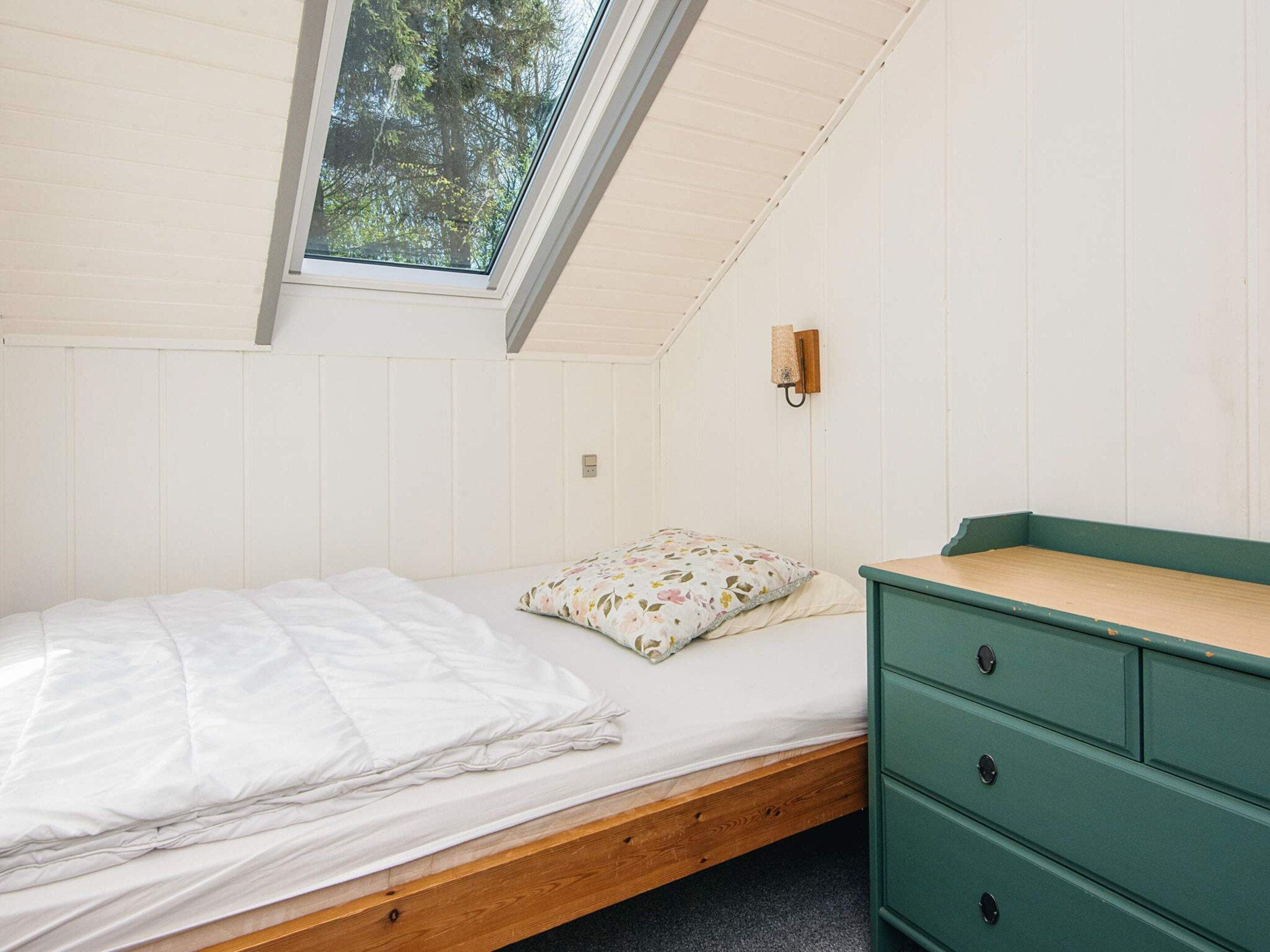 A single-bed room with a skylight, a wooden headboard, a green dresser, and a floral pillow.
